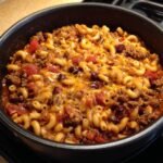Close-up of Savory Hobo Casserole Ground Beef mixture with macaroni, beans, and melted cheese in a black cooking pot.