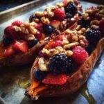 Two baked sweet potato halves filled with mixed berries, walnuts, and drizzled with syrup for Sweet Potato Berry Breakfast Boats.