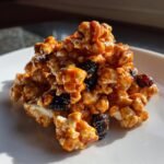 A close-up of Tempting Creepy Caramel Candy Popcorn mixed with dark dried fruit, piled on a white plate.