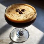 A rich, dark Vegan Espresso Martini Mocktail topped with creamy foam and three coffee beans.