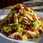A vibrant chicken Brussels sprout salad recipe mound featuring shredded chicken, halved sprouts, pecans, and dried cranberries.