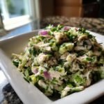 Close-up of Zesty Cilantro Lime Chicken Salad with shredded chicken, green herbs, and red onion pieces in a white bowl.