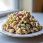 A mound of Zesty Dill Pickle Pasta Salad featuring elbow macaroni, red onion, green pepper, and creamy dill dressing on a white plate.