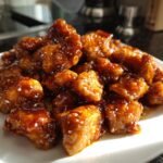 A close-up of sticky, glazed pieces of 15 Minute Easy Orange Chicken sprinkled with sesame seeds on a white plate.