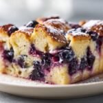 A close-up of a square slice of Irresistible Blueberry French Toast Casserole, topped with powdered sugar.