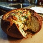 A close-up of a Cheesy Seafood Bread Bowl Delight, featuring melted cheese, shrimp, and parsley topping in a hollowed-out loaf.