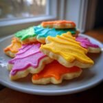 A stack of brightly colored, tree-shaped Irresistible Holiday Sugar Cookies with vibrant icing on a white plate.