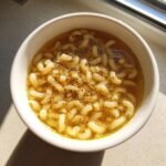 A close-up of a white bowl filled with Comforting Pastina Soup, seasoned with pepper.