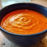Close-up of a vibrant orange, creamy Tomato Bisque Recipe swirled in a dark blue bowl.