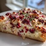 A thick slice of Irresistible Cranberry Chicken Brie Pizza showing melted cheese, chicken, red onions, and cranberries.