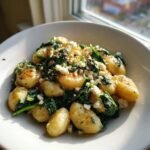 A close-up of creamy gnocchi with spinach and feta bliss served in a white bowl near a window.
