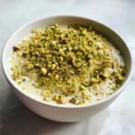 A white bowl filled with creamy Pistachio Overnight Oats Recipe, generously topped with chopped green pistachios.
