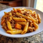 A close-up of a white bowl filled with Creamy Sausage Pasta With Sweet Potato, featuring penne pasta and ground sausage in a rich sauce.