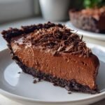 A close-up of a rich slice of Decadent French Silk Pie with a thick chocolate mousse filling and chocolate shavings on top.