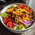 Close-up of Delicious Burger Bowls featuring seasoned ground beef, cheddar cheese, tomatoes, and red onion on lettuce.