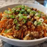 Close-up of a white bowl filled with Delicious Egg Roll In A Bowl Recipe, topped with ground meat, sauce, and green onions.