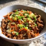 A close-up of a white bowl filled with a Delicious Egg Roll In A Bowl Recipe, featuring ground meat, shredded cabbage, carrots, and green onions.