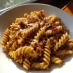 A close-up of a bowl of French Onion Pasta Recipe featuring fusilli pasta coated in a rich sauce, topped with melted cheese and caramelized onions.