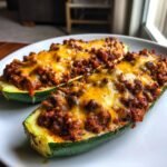 Two Delicious Ground Turkey Taco Stuffed Zucchini Boats topped with melted cheddar cheese on a white plate.