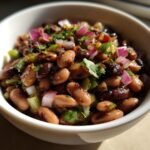 Close-up of a Delicious Miso Sesame Dense Bean Salad with red onion and herbs in a white bowl.