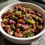 Close-up of a Delicious Miso Sesame Dense Bean Salad mixed with red onion and cilantro in a white bowl.