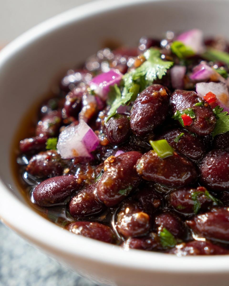 Close-up of Delicious Miso Sesame Dense Bean Salad featuring dark red beans coated in a rich sauce with diced red onion and cilantro.