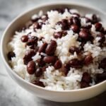 Close-up of a white bowl filled with fluffy white rice mixed with dark, seasoned black beans for a Delicious Rice And Beans recipe.