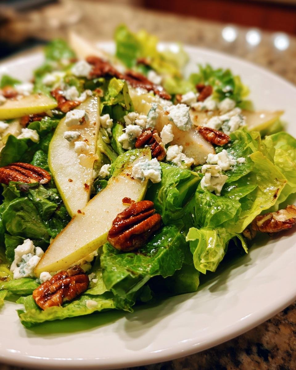 Close-up of a Delightful Autumn Salad With Pear And Goat Cheese Recipe, featuring lettuce, sliced pears, crumbled blue cheese, and candied pecans.