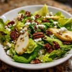 Close-up of a Delightful Autumn Salad With Pear And Goat Cheese, featuring crisp lettuce, pear slices, pecans, and crumbled blue cheese.