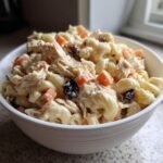 Close-up of a white bowl filled with Delightful Filipino Chicken Macaroni Salad, featuring creamy sauce, elbow macaroni, shredded chicken, carrots, and raisins.