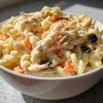 Close-up of Delightful Filipino Chicken Macaroni Salad with shredded chicken, carrots, and raisins in a white bowl.