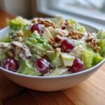 A white bowl filled with a Delightful Waldorf Salad Recipe featuring grapes, apples, walnuts, and creamy dressing.