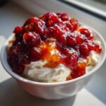 Close-up of Festive Cranberry Orange Cream Cheese Dip topped with glistening cranberry sauce in a white bowl.