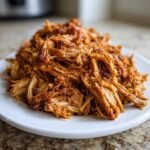 A close-up of shredded, saucy Flavorful Crockpot Carnitas piled high on a white plate, ready to serve.