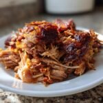 Close-up of tender, shredded Flavorful Crockpot Carnitas Recipe with crispy, caramelized edges on a white plate.