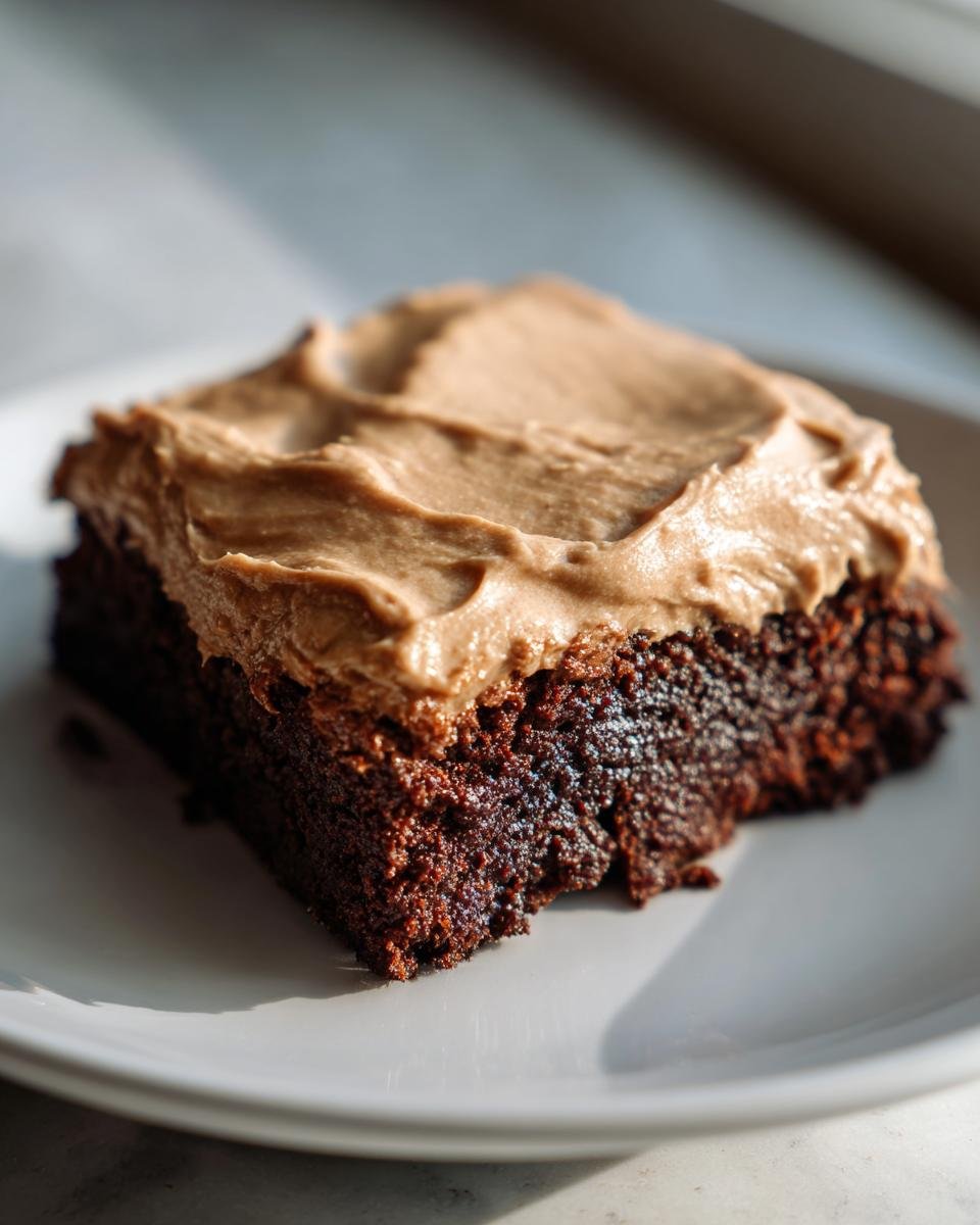 A close-up of a single, rich, dark chocolate brownie topped with thick coffee frosting.