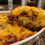 A spoonful being lifted from a baked Hearty Ground Beef Potatoes Casserole, showing layers of meat, potatoes, and melted cheese.