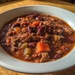 A close-up of a white bowl filled with rich, thick Hearty Hobo Stew featuring ground meat, kidney beans, and chunks of carrots.