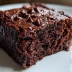 A moist, rich square of Indulgent Sweet Potato Brownies topped with melted chocolate chips on a white plate.