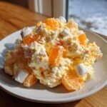 A scoop of creamy, fluffy Irresistible Ambrosia Salad featuring mandarin orange segments and mini marshmallows on a white plate.