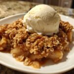A warm serving of Irresistible Apple Crisp Recipe topped with a scoop of vanilla ice cream on a white plate.