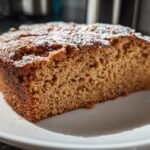 Close-up of a moist slice of Irresistible Applesauce Cake dusted with powdered sugar on a white plate.