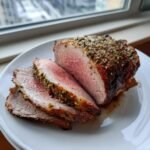 Slices of perfectly roasted, medium-rare Irresistible Boneless Leg Of Lamb seasoned with herbs.