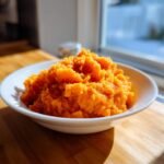 A close-up of bright orange, fluffy Irresistible Bourbon Brown Sugar Sweet Potato Mash served in a white bowl.