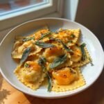 A white bowl filled with Irresistible Butternut Squash Sage Ravioli topped with browned butter sauce and fresh sage leaves.