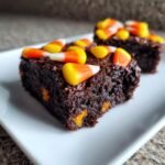 Close-up of fudgy Irresistible Candy Corn Brownies topped with colorful candy corn pieces on a white plate.