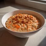 A bowl of Irresistible Carrot Cake Overnight Oats topped with shredded carrots, walnuts, and cinnamon.