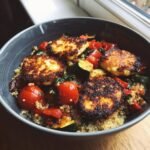 Close-up of an Irresistible Charred Vegetable Halloumi Grain Bowl featuring seared halloumi, cherry tomatoes, zucchini, and quinoa.