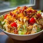 A close-up of an Irresistible Chicken Bacon Ranch Bowls recipe, topped with shredded chicken, cheese, bacon, and tomatoes.