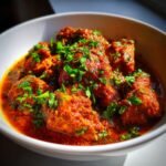 A close-up shot of rich, red Irresistible Chicken Masala served in a white bowl and garnished with fresh chopped cilantro.